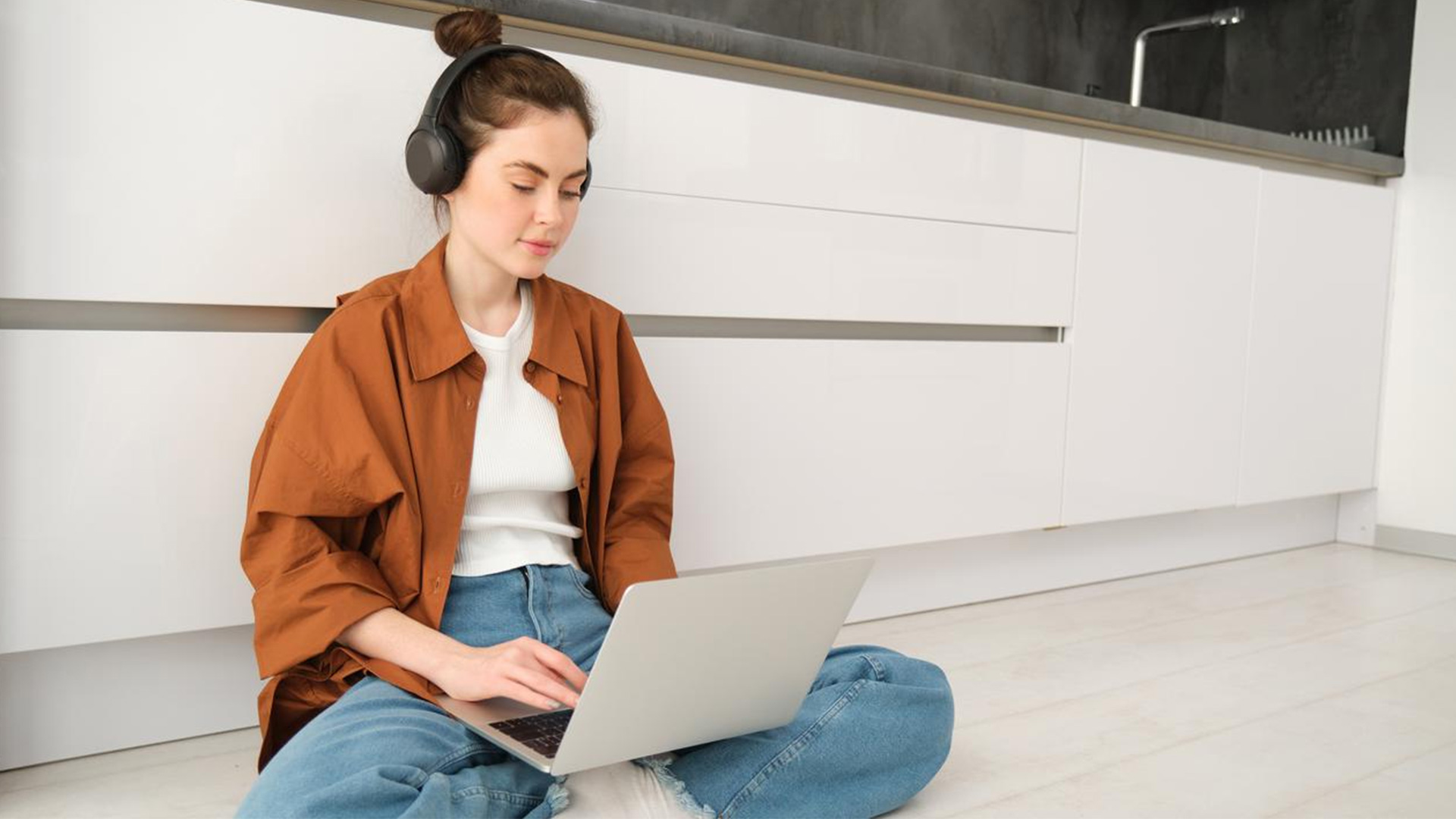 Frau sitz mit Laptop am Boden in der Küche. 