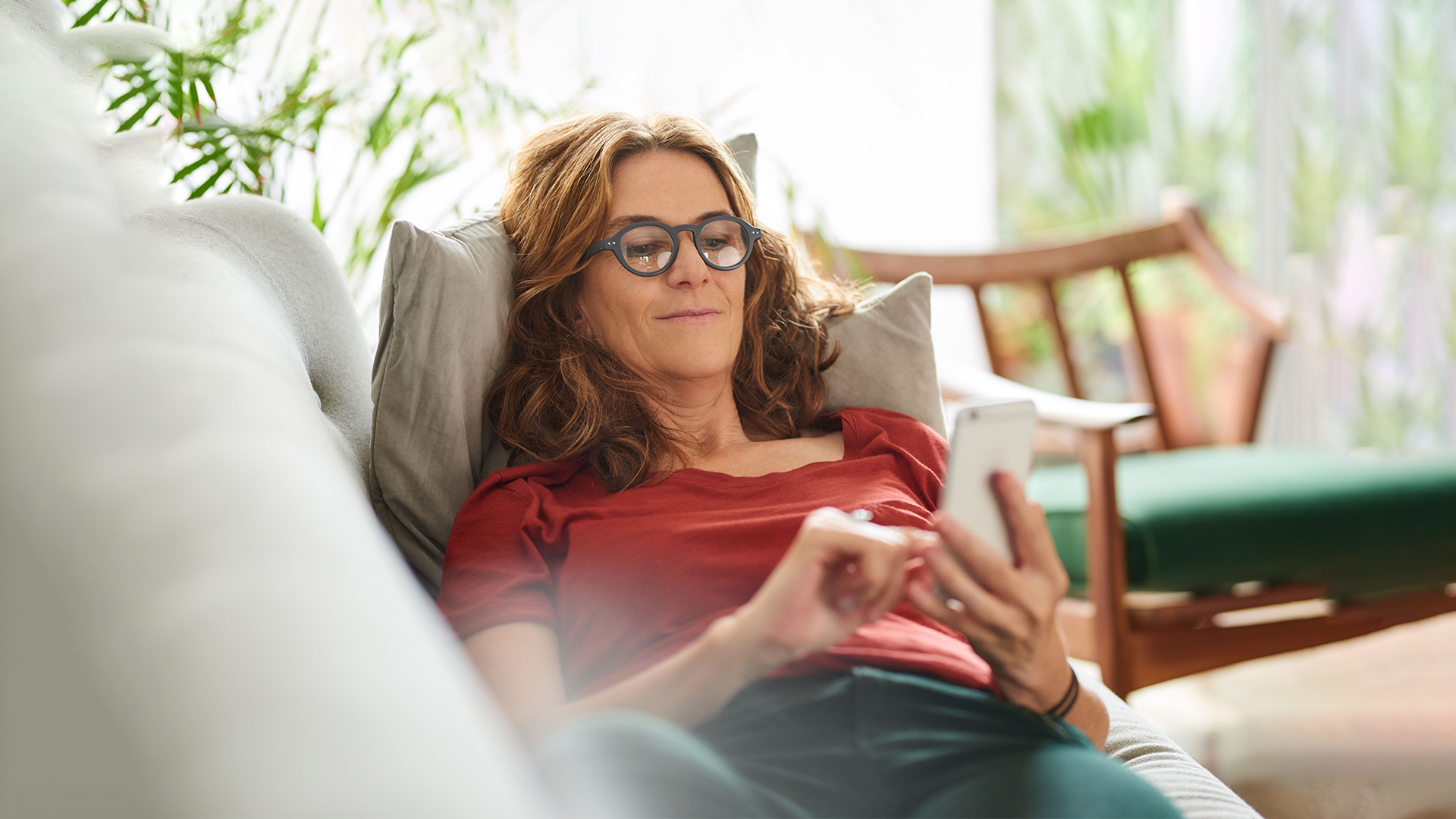 Frau mit Smartphone in der Hand auf Couch. 