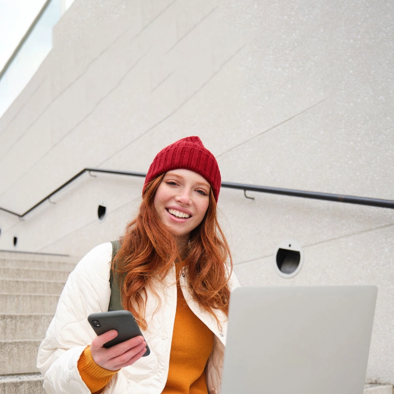 Junge Frau sitzt mit Smartphone und Laptop auf einer Treppe. Junge Frau sitzt mit Smartphone und Laptop auf einer Treppe.