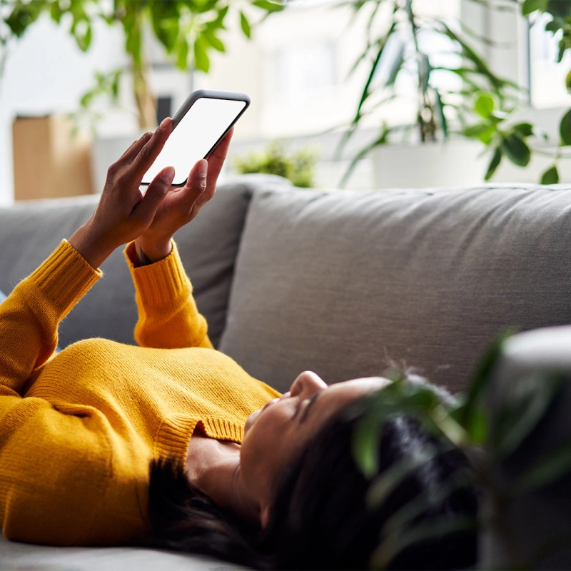 Frau liegt mit Smartphone in der Hand auf der Couch. Frau liegt mit Smartphone in der Hand auf der Couch.
