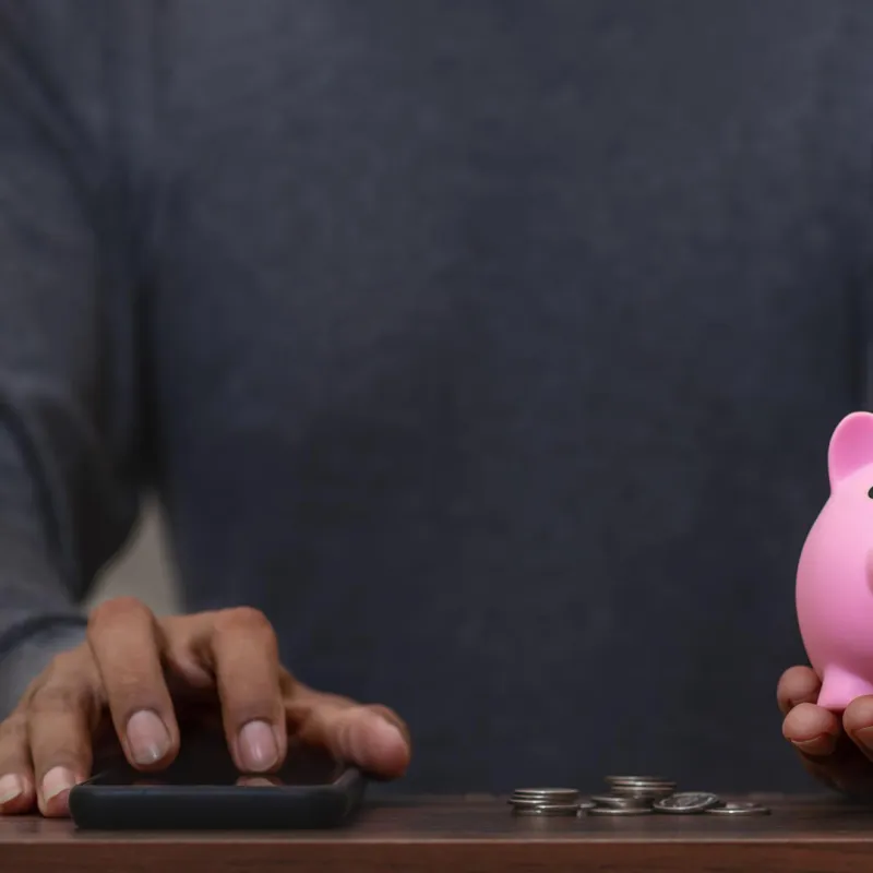 Person mit Smartphone und Sparschwein.